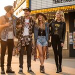 Skupina mladých ľudí v bežnom oblečení pred hudobným klubom za západu slnka.